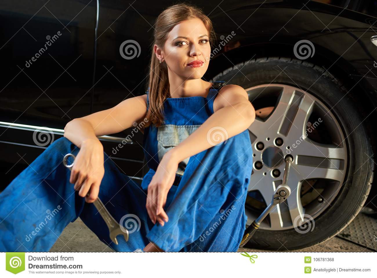 female-mechanic-blue-suit-sits-near-tire-holding-wrench-female-mechanic-sits-near-tire-holding...jpg
