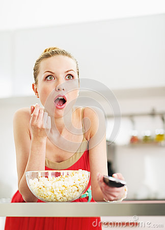 surprised-young-woman-eating-popcorn-watching-tv-kitchen-modern-32745032.jpg